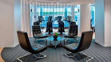 A conference room with four black chairs around a central table, a large window with a view of outdoor exercise equipment, and a modern interior design.
