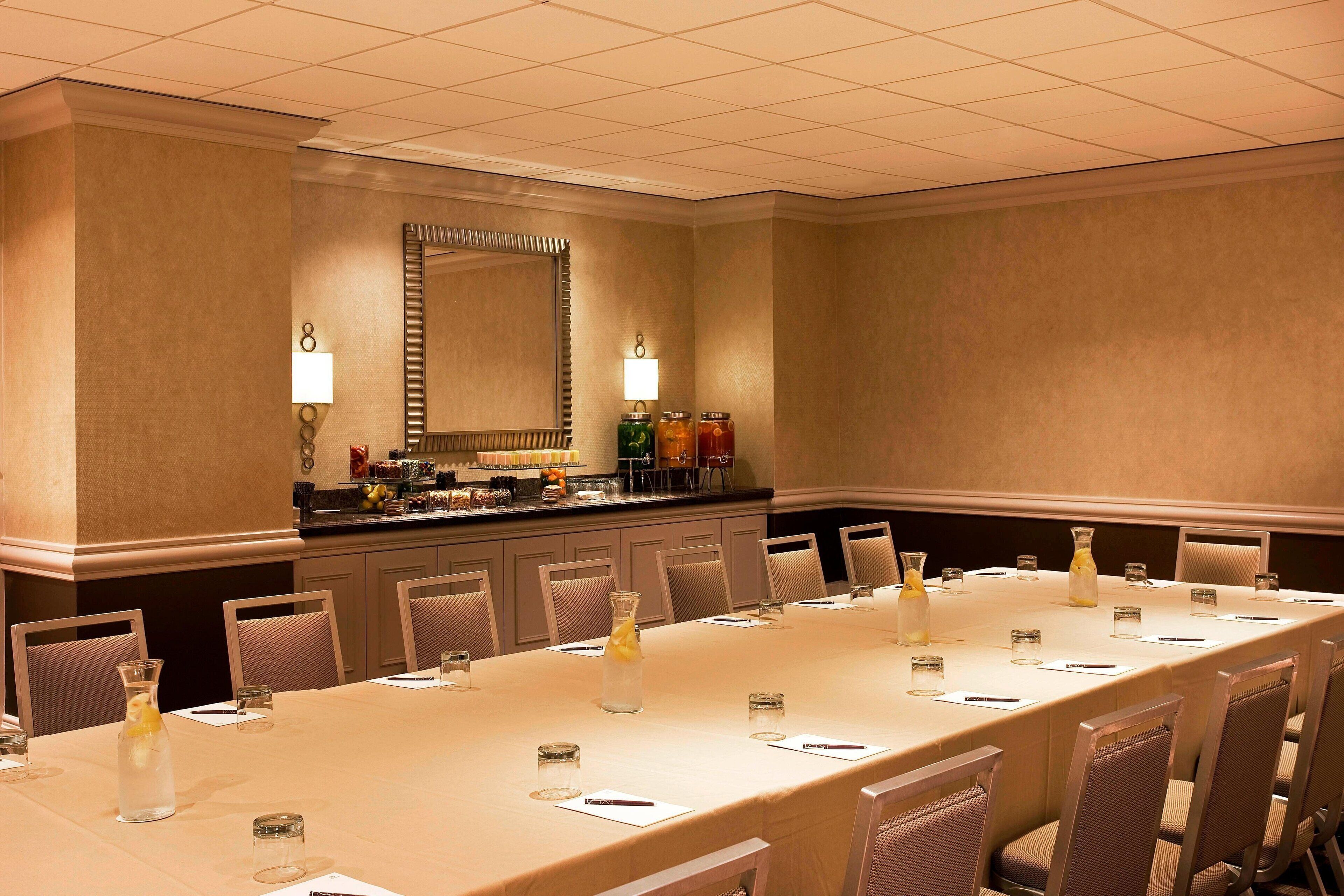 A conference room with a long table, chairs, a bar area, and a large mirror.
