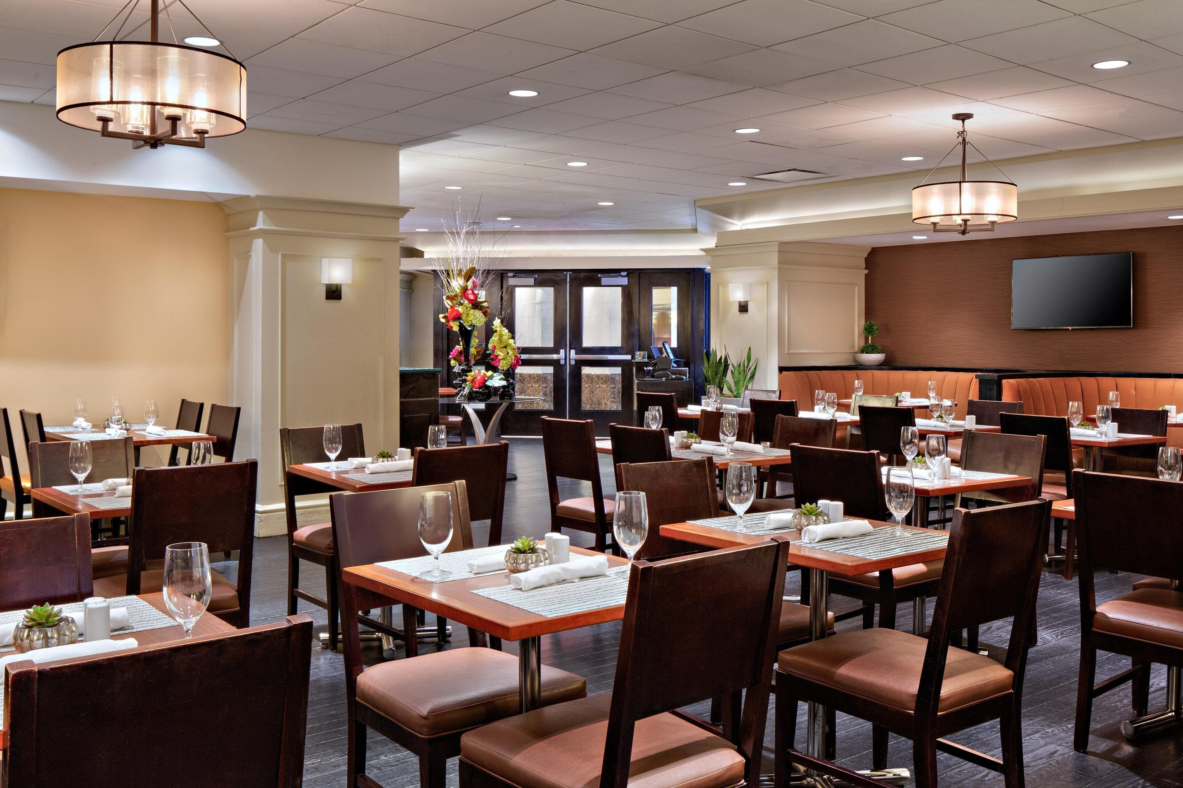 A restaurant with multiple tables and chairs, a chandelier, and a television mounted on the wall.