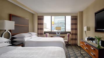 A hotel room with two beds, a desk, a chair, a TV, and a view of the city.