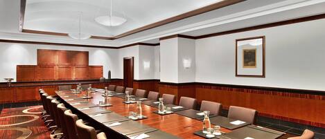 Un salón de conferencias con una larga mesa, varias sillas y una pared de madera decorativa.