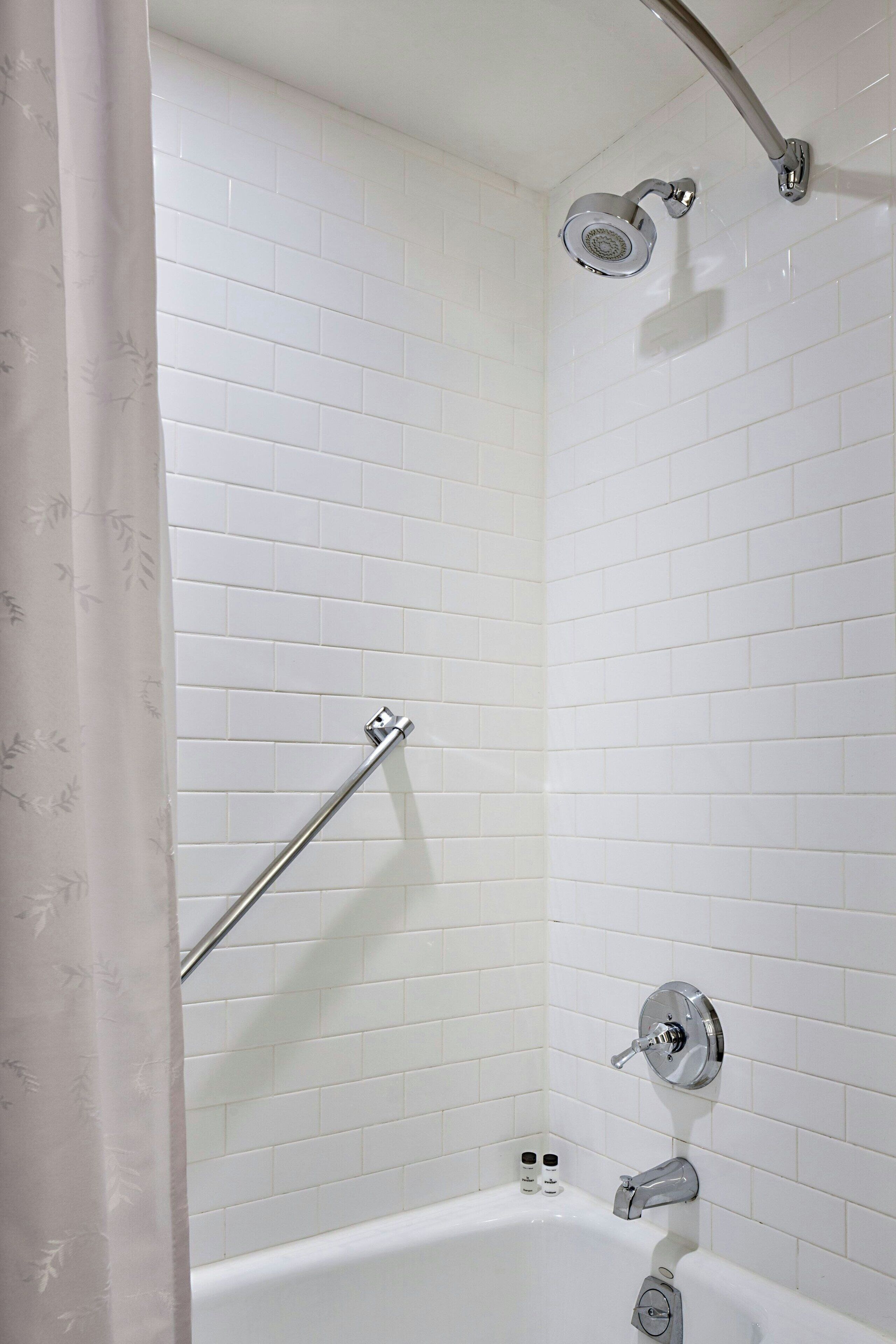 Ein modernes Badezimmer mit weiß gefliesten Wänden, einer Duschbrause, einer Haltestange und einer Badewanne.
