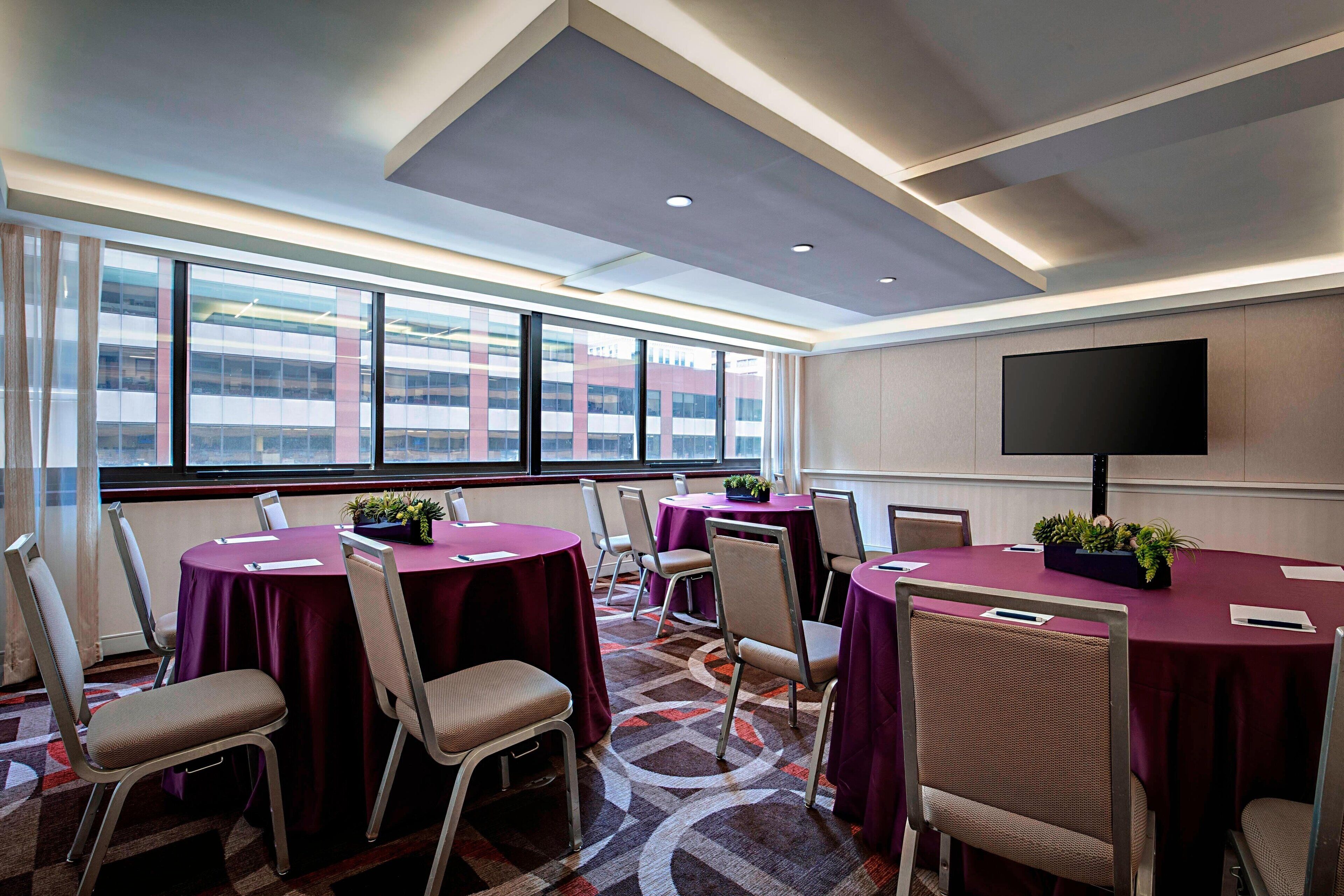 A conference room with round tables, chairs, and a large window with a city view.