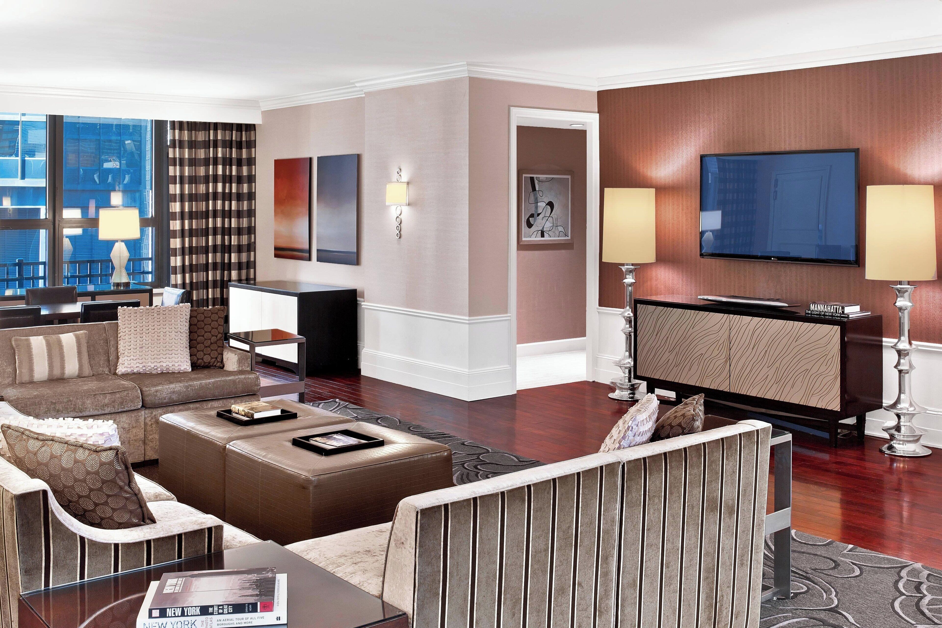 A modern hotel room with a living area featuring a sofa set, a coffee table, and a flat-screen TV mounted on the wall.
