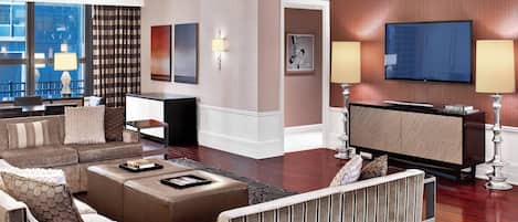 A modern hotel room with a living area featuring a sofa set, a coffee table, and a flat-screen TV mounted on the wall.