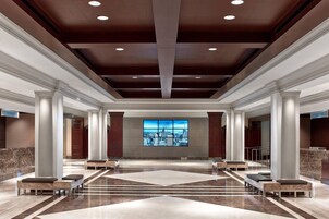 A spacious lobby with marble flooring, large columns, and a cityscape view through a large window.