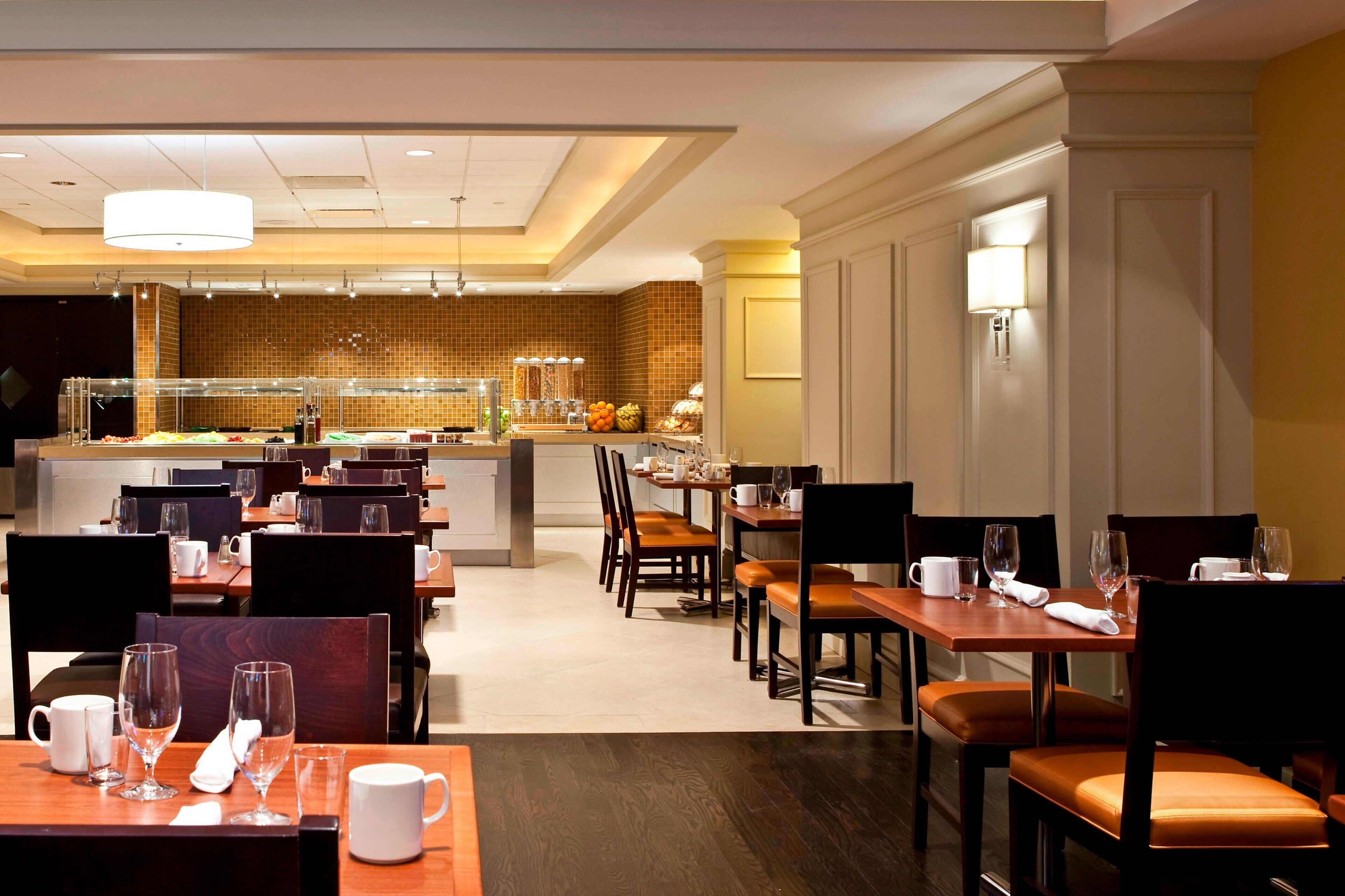 A hotel dining area with multiple tables and chairs, a buffet counter in the background, and a modern interior design.