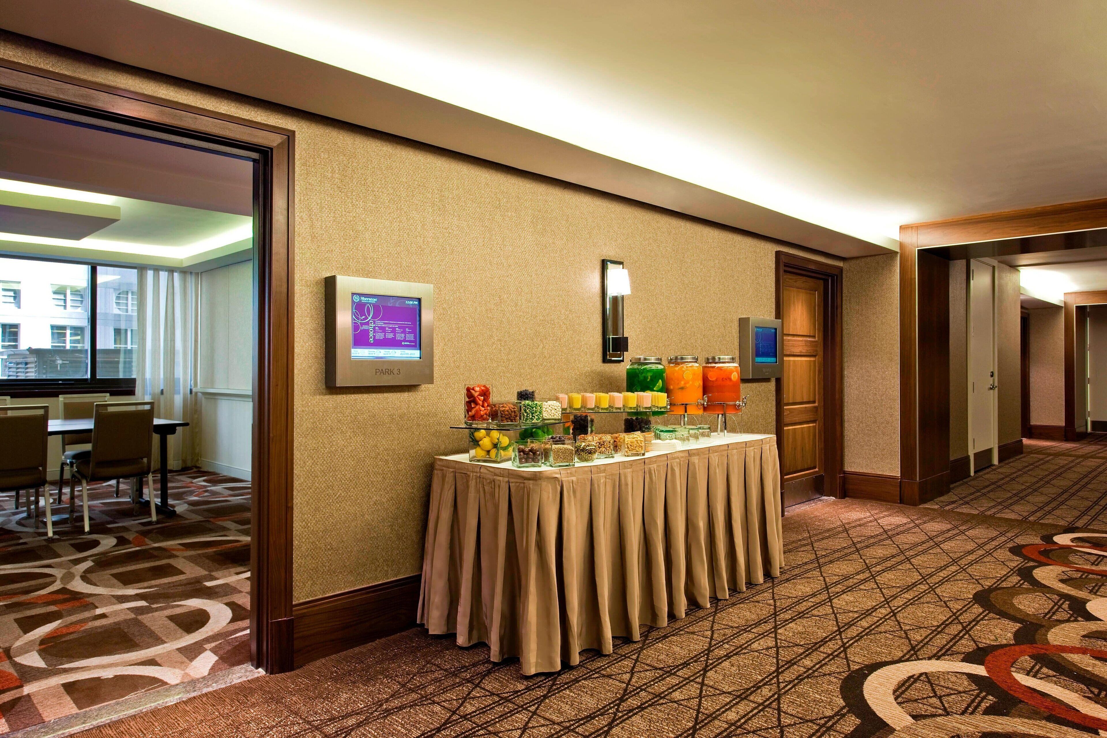 Vestíbulo de hotel con una mesa de buffet, una pantalla digital y una alfombra estampada.