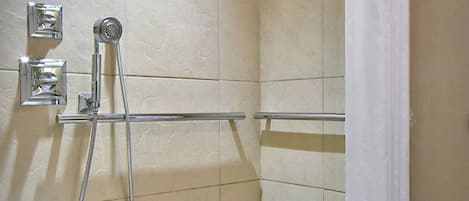 A small, tiled shower area with a white shower chair, a handheld showerhead, and a white shower curtain.