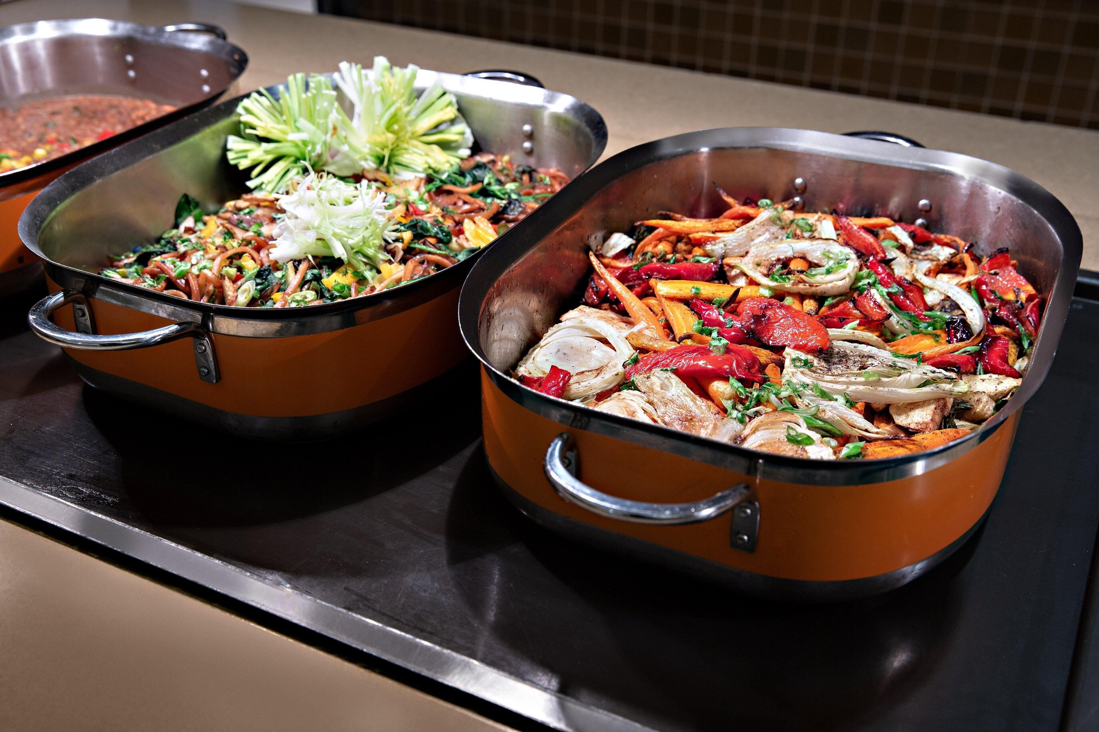 Two large metal pots filled with various vegetables and meats on a kitchen counter.