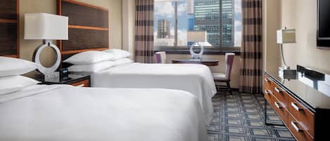 Habitación de hotel con dos camas, un escritorio, una silla, un televisor y una ventana con vista a la ciudad.