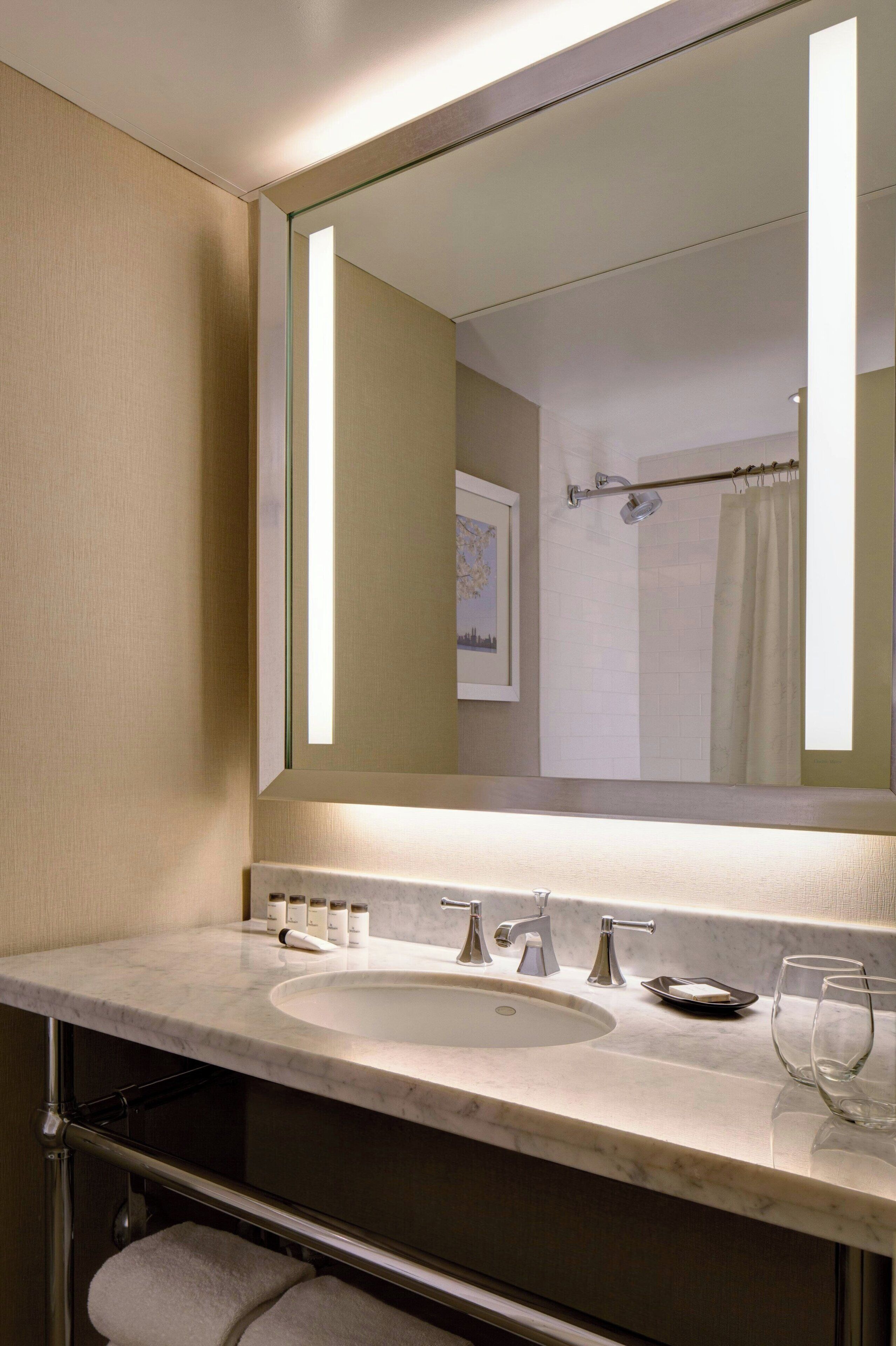 A modern bathroom with a large mirror, a sink, and a shower area.