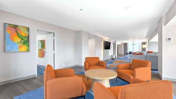 Un moderno vestíbulo de hotel con sillones naranjas, una mesa redonda y obras de arte en las paredes.