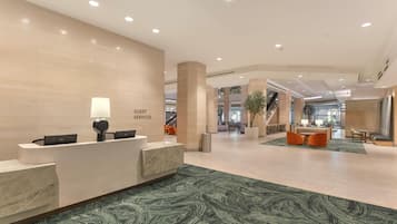 Zona de recepción de hotel con mostrador de mármol, cartel de servicios para huéspedes y alfombra estampada verde.