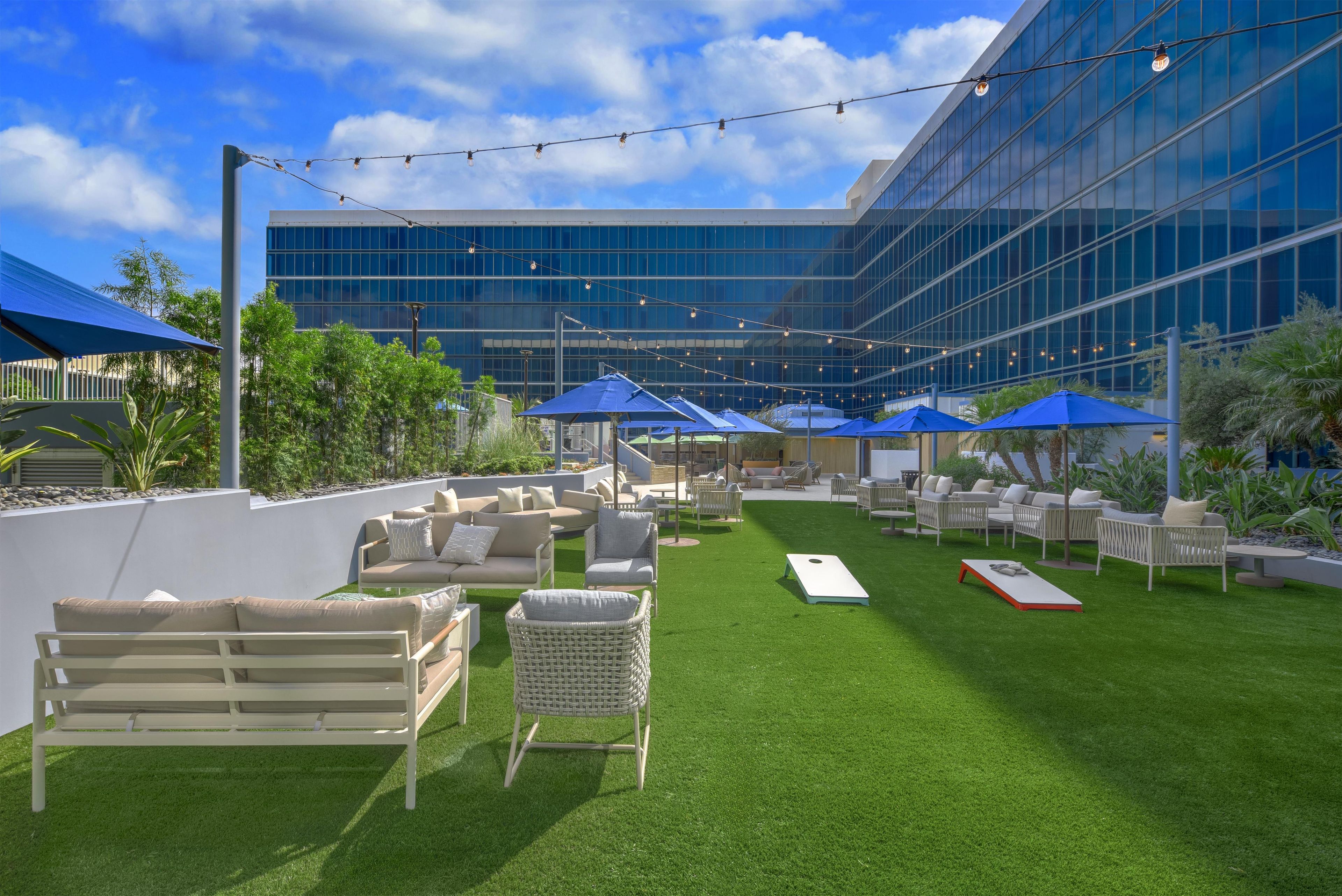 An outdoor seating area with artificial grass, wicker furniture, and blue umbrellas.