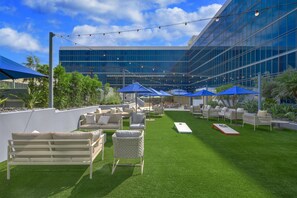 Un espace extérieur aménagé avec du gazon synthétique, des meubles en osier et des parasols bleus.