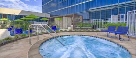 A hot tub area with a pool, lounge chairs, and umbrellas.