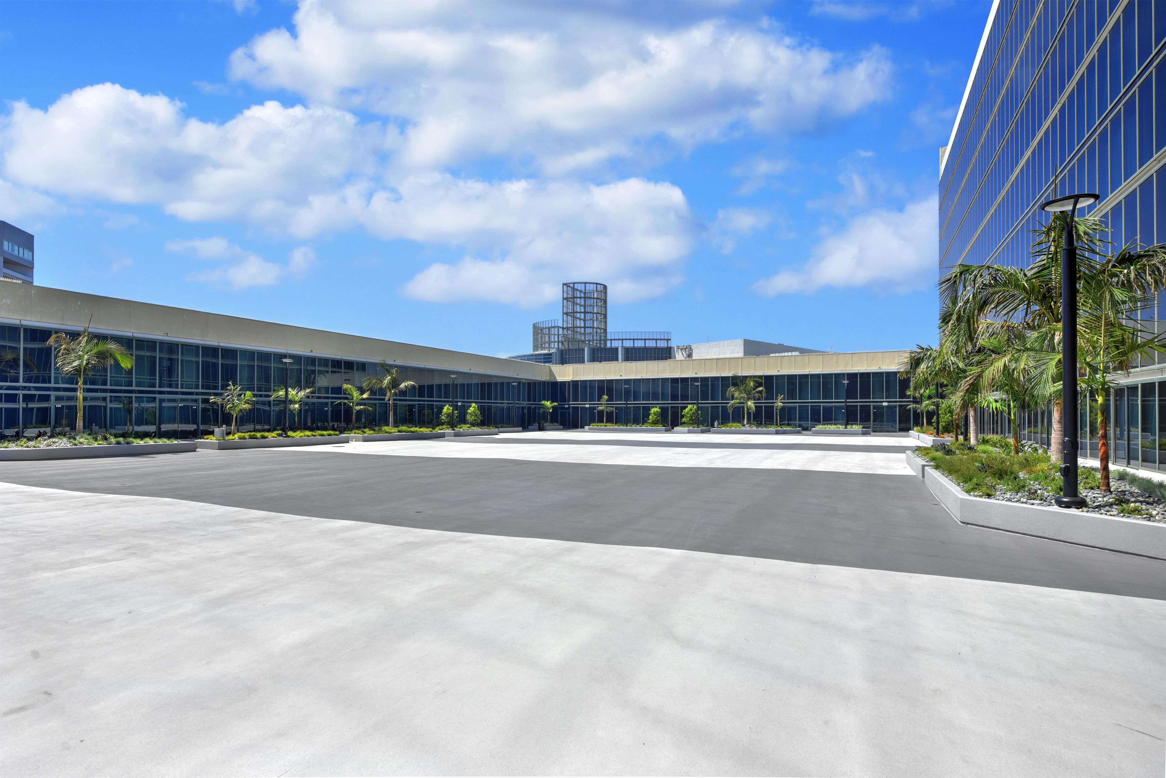 A modern building with a glass facade, a spacious courtyard, and palm trees.