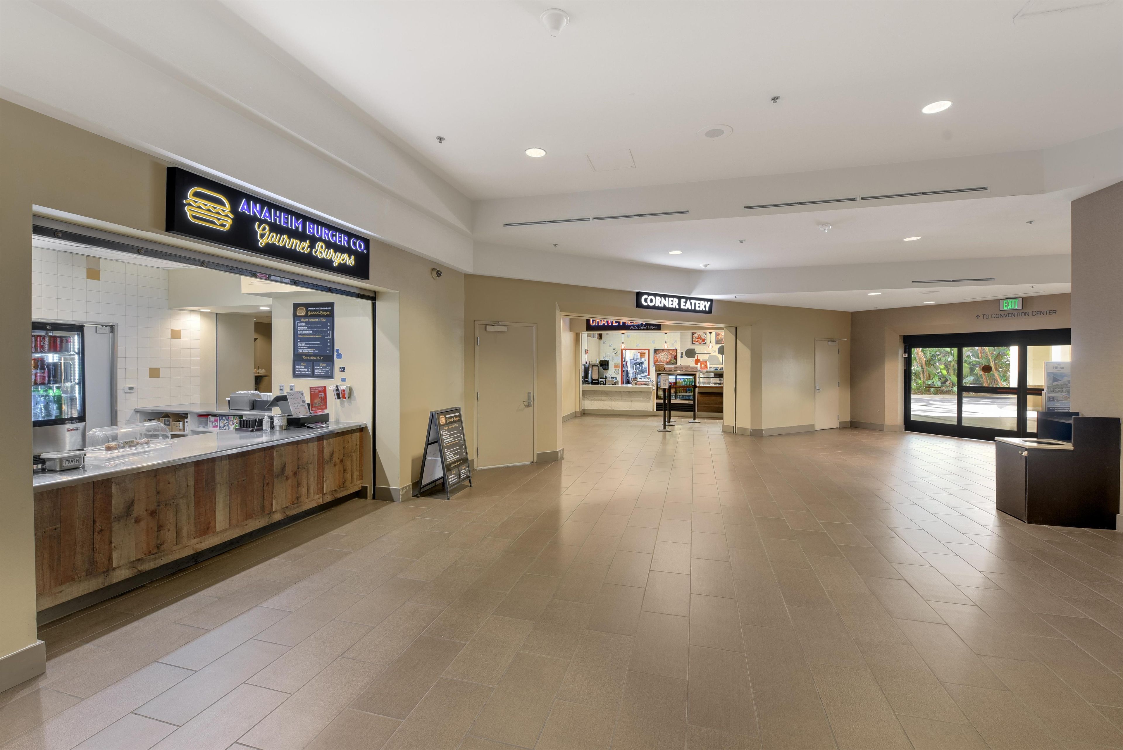 A spacious indoor area with a food counter, a sign for 'Corner Eatery', and an exit sign indicating the direction to the convention center.