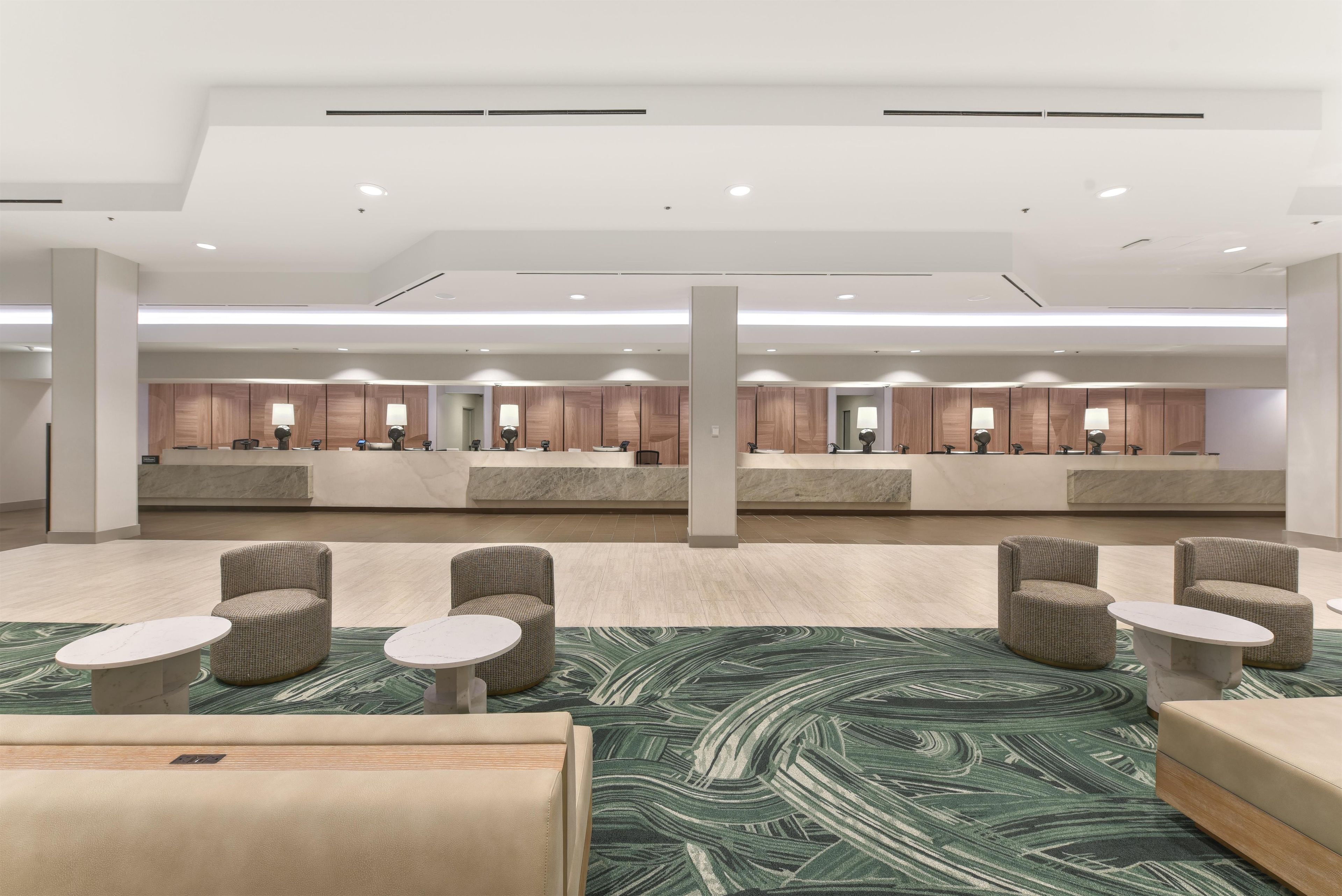 Eine Hotelhalle mit mehreren Rezeptionen, Sitzbereichen und einem gemusterten Teppich.