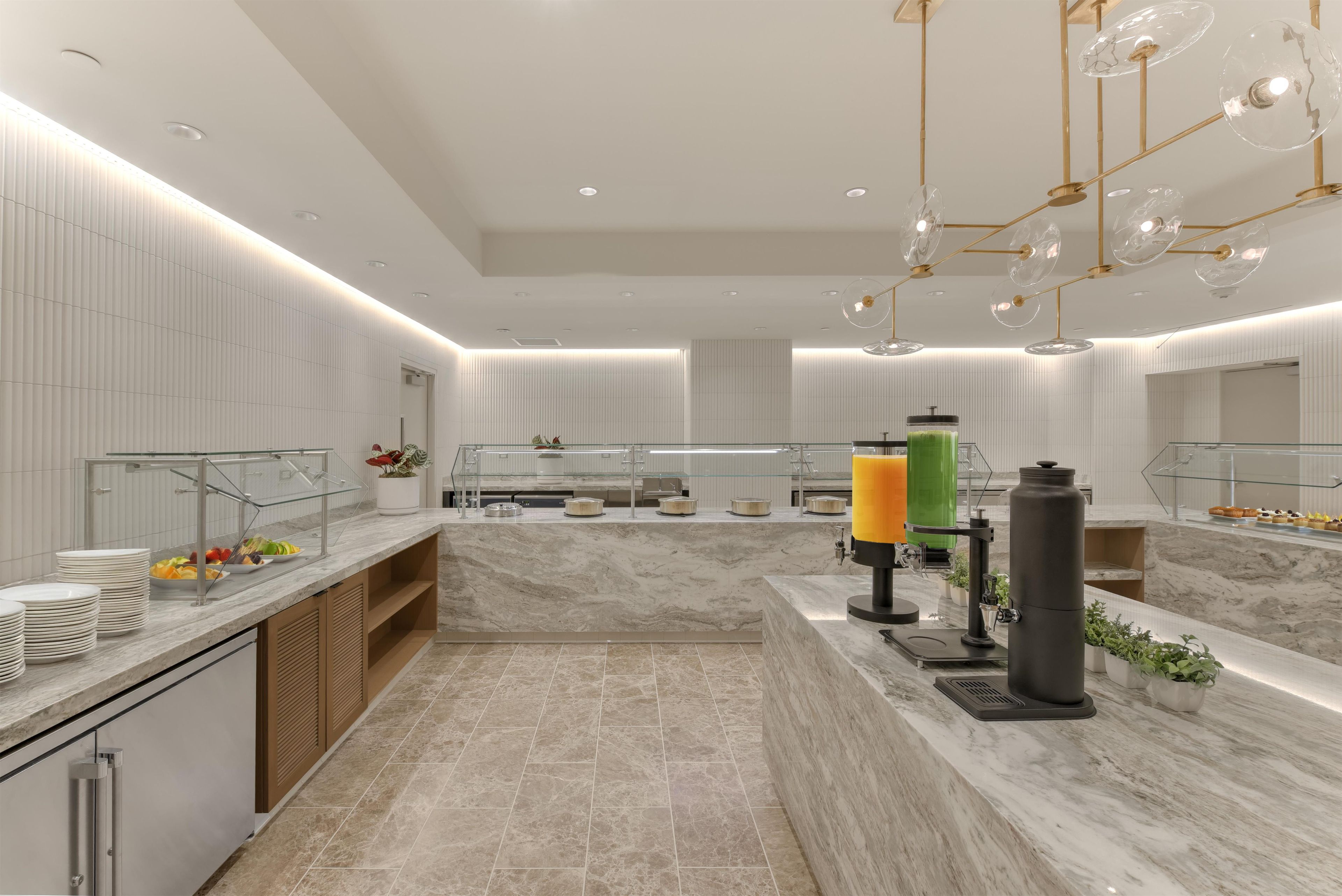 Une cuisine moderne avec des plans de travail en marbre, un meuble vitrine et un distributeur de jus.