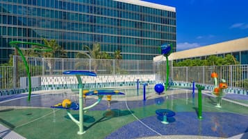 Zona de juegos al aire libre con diferentes fuentes de agua y un edificio moderno al fondo.