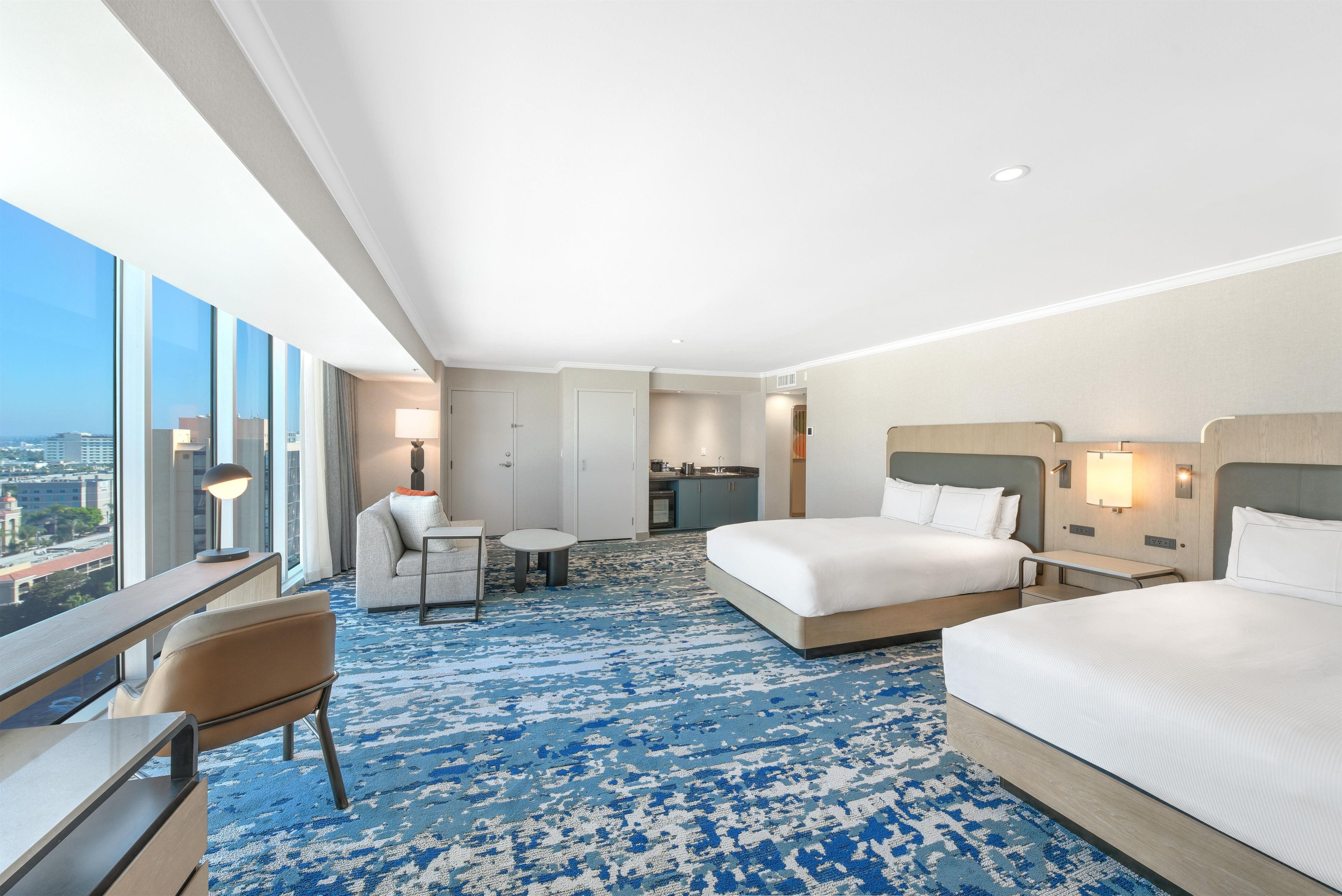 A hotel room with a large bed, a desk, a chair, and a view of the city.