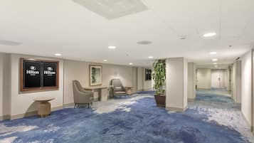 Un hall de hotel con alfombra azul, zona de estar y una planta grande en maceta.
