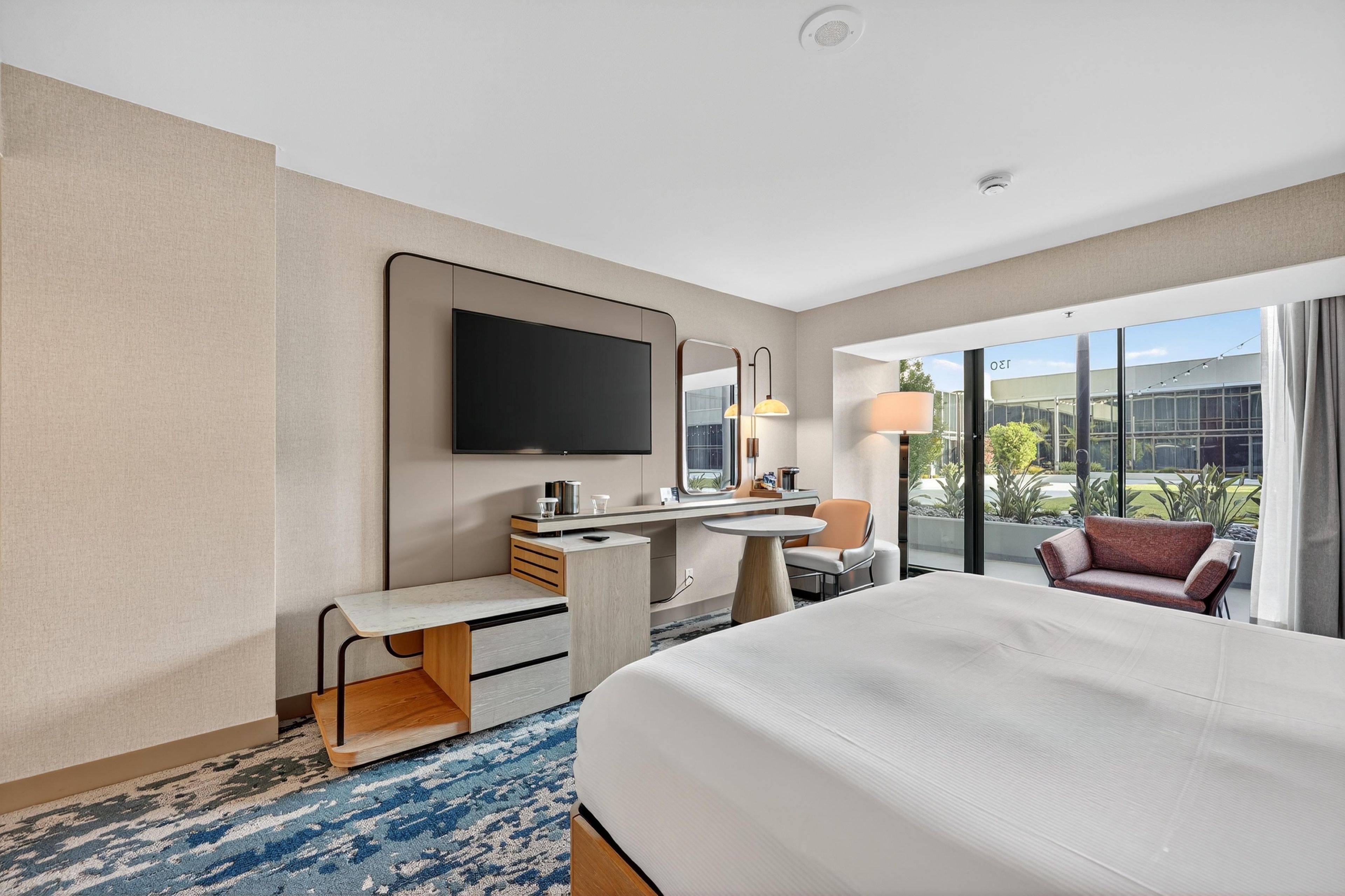 A hotel room with a large bed, a desk, a chair, a television, and a view of the outdoors.