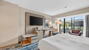 A hotel room with a large bed, a desk, a chair, a television, and a view of the outdoors.