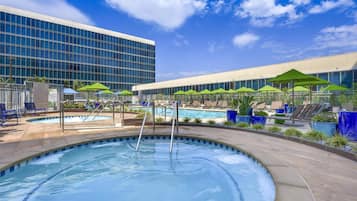 A swimming pool area with lounge chairs and umbrellas, surrounded by modern buildings.
