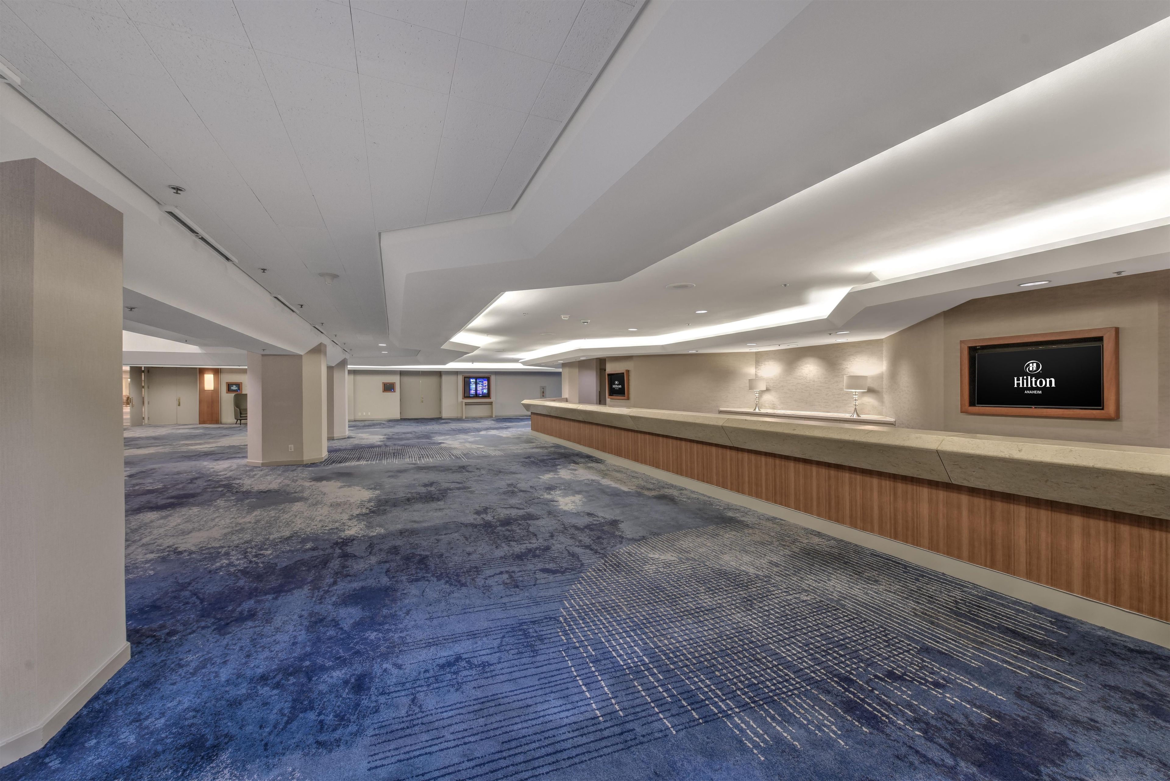 A hotel lobby with a reception desk, a digital screen, and a carpeted floor.