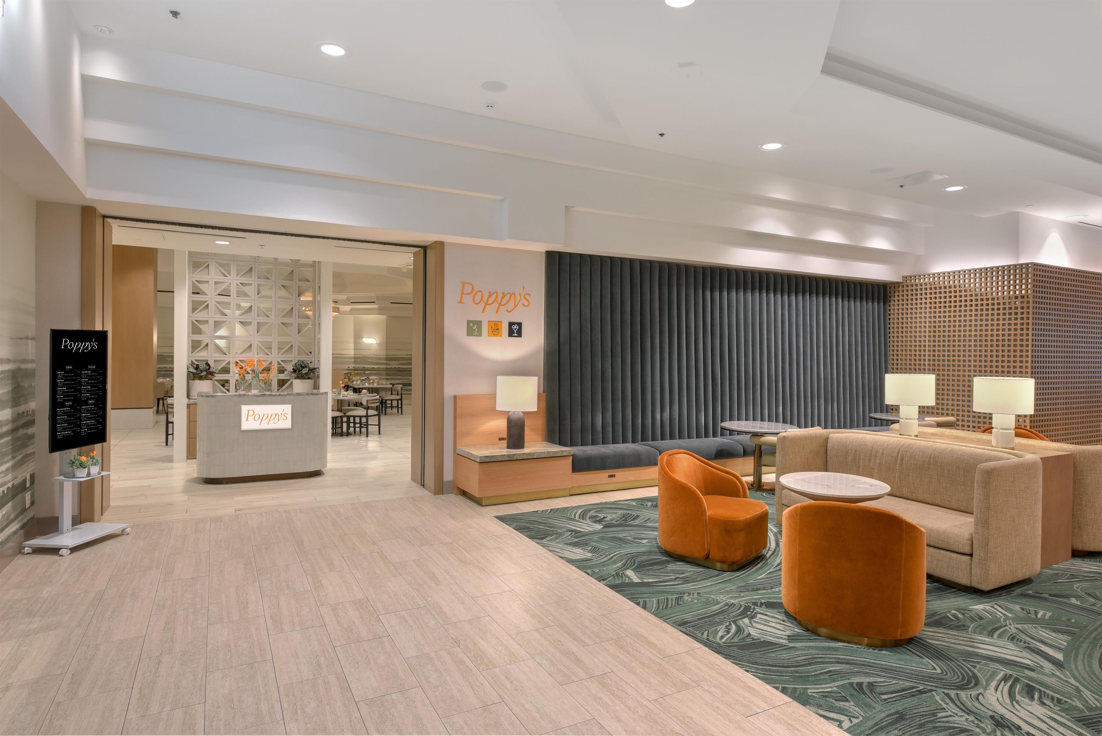 A modern hotel lobby with a reception desk, seating area, and a view into the dining area.