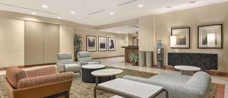 A hotel lobby with seating areas, a reception desk, and framed artwork on the walls.