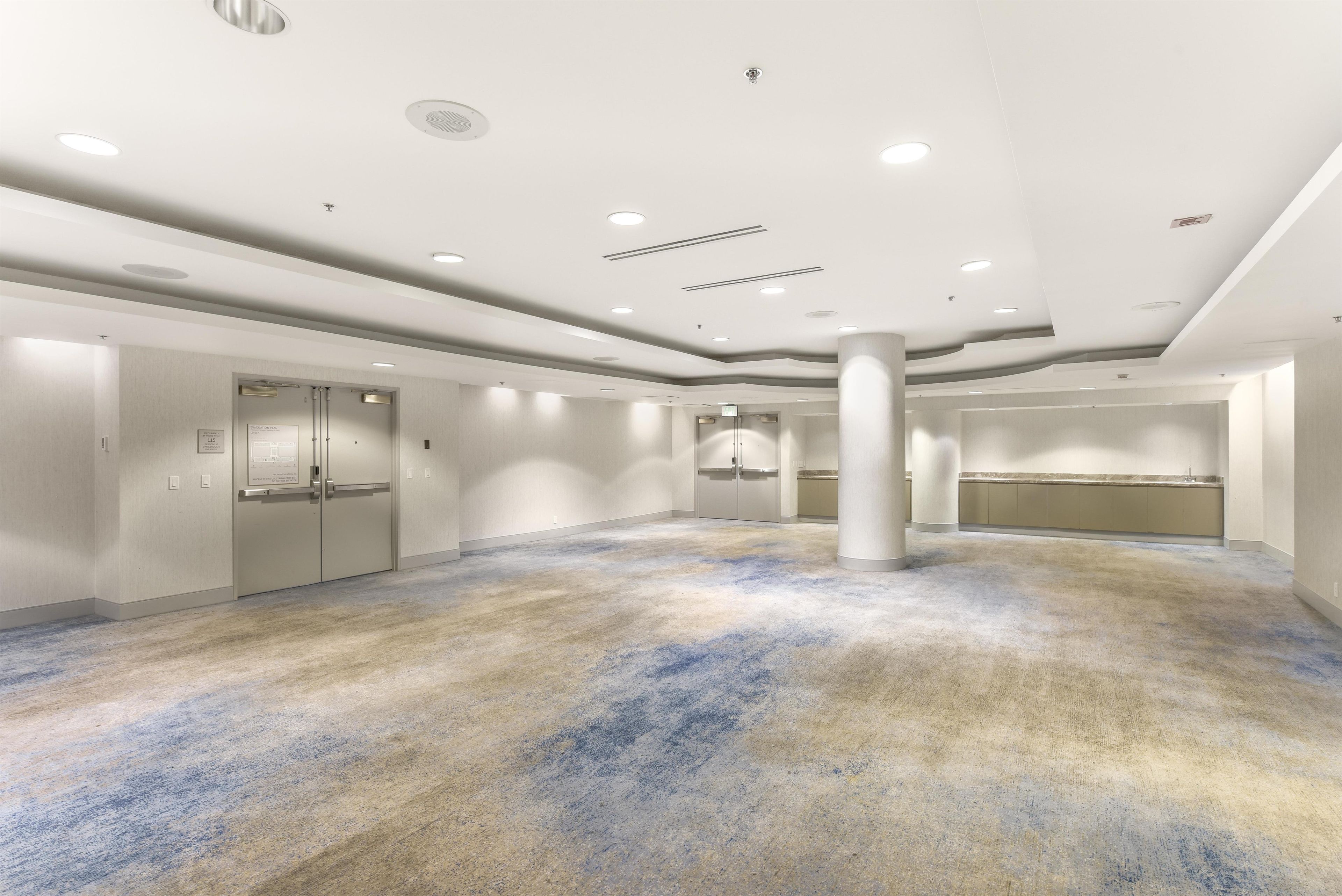 A spacious hotel lobby with a high ceiling, recessed lighting, and a carpeted floor.