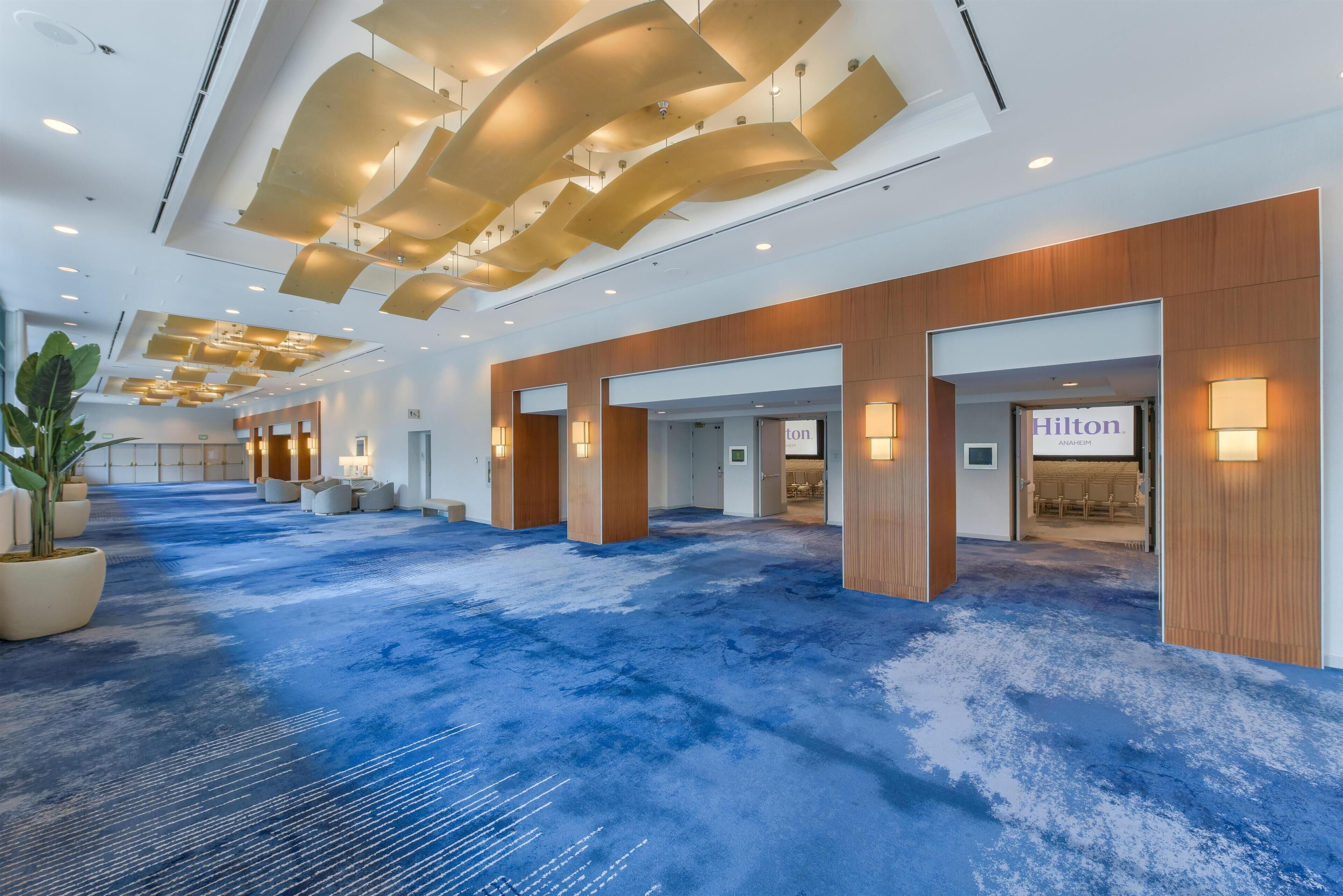 A spacious lobby with a blue carpet, wooden accents, and illuminated signs for Hilton Anahuac.