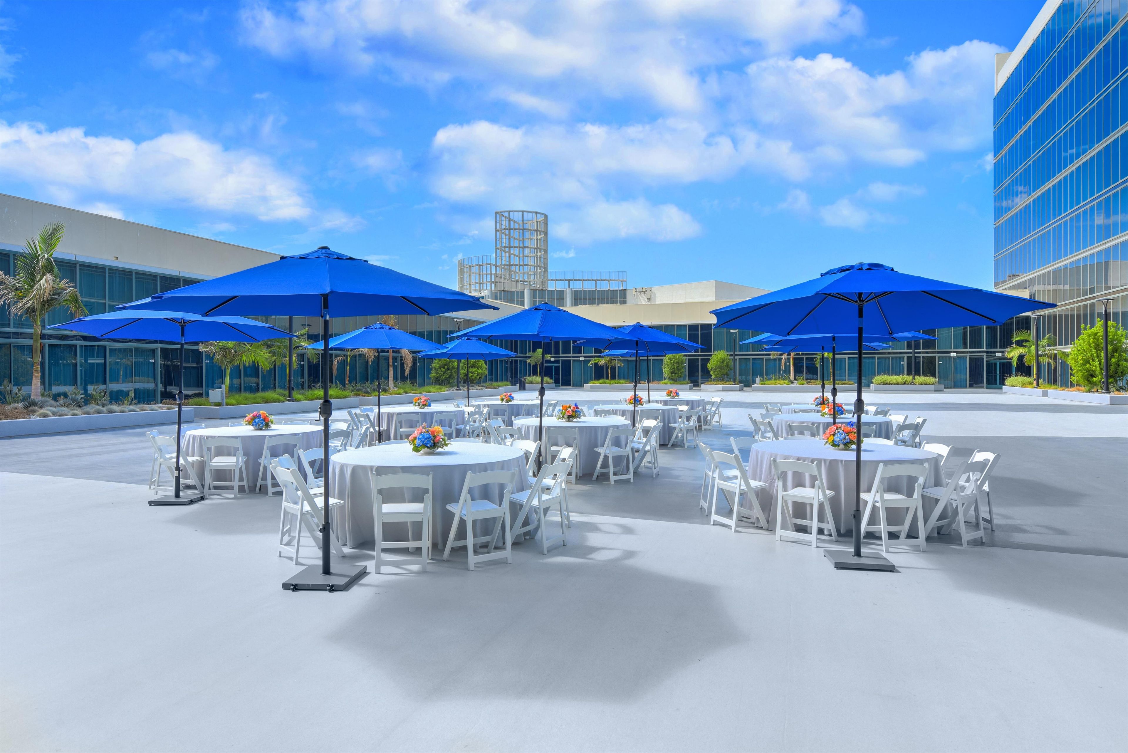 An outdoor seating area with round tables, white chairs, and blue umbrellas.
