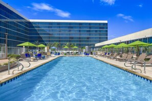 A swimming pool with lounge chairs and umbrellas, surrounded by a modern building.
