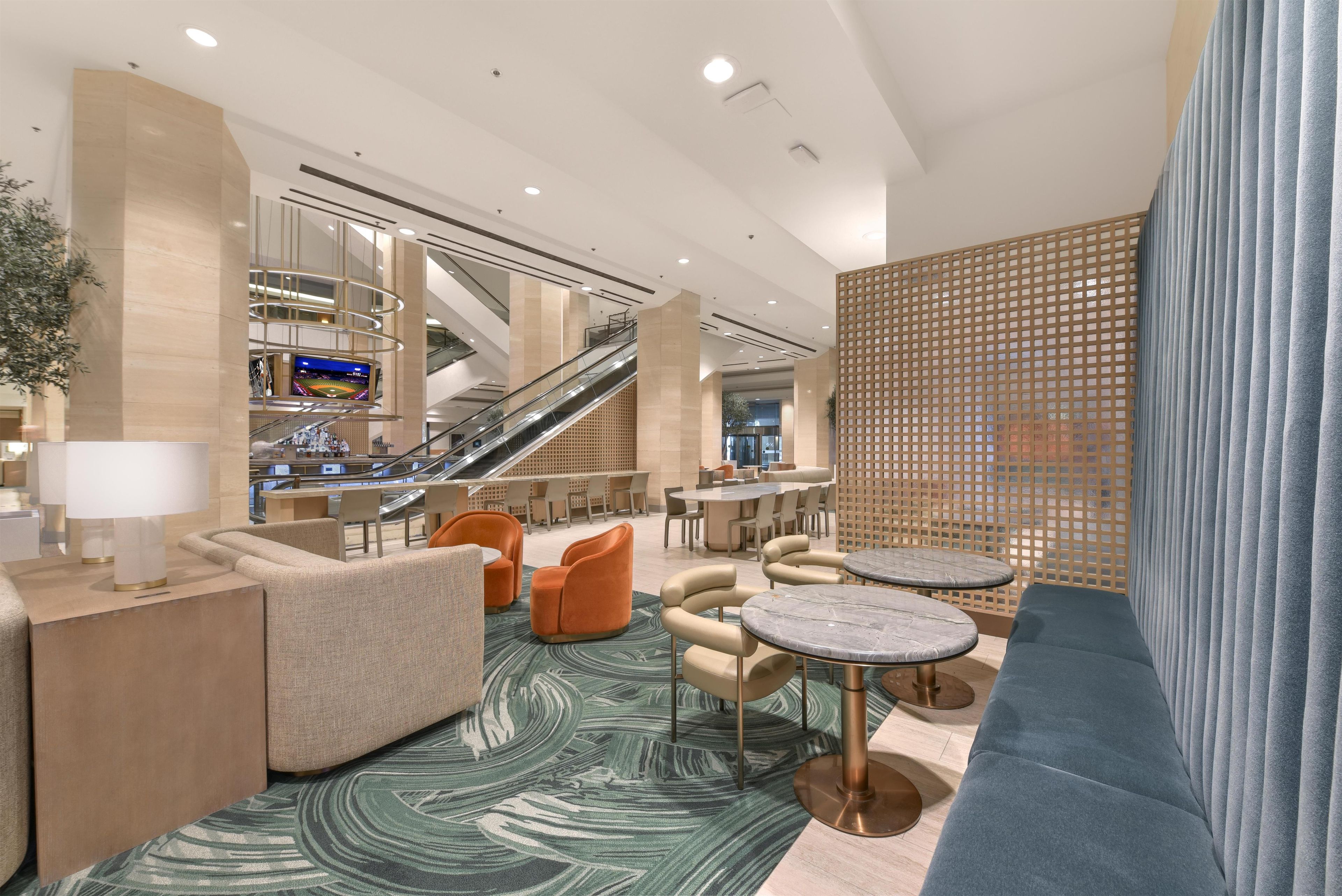 A modern hotel lobby with a seating area, a staircase, and a large screen displaying a sports event.