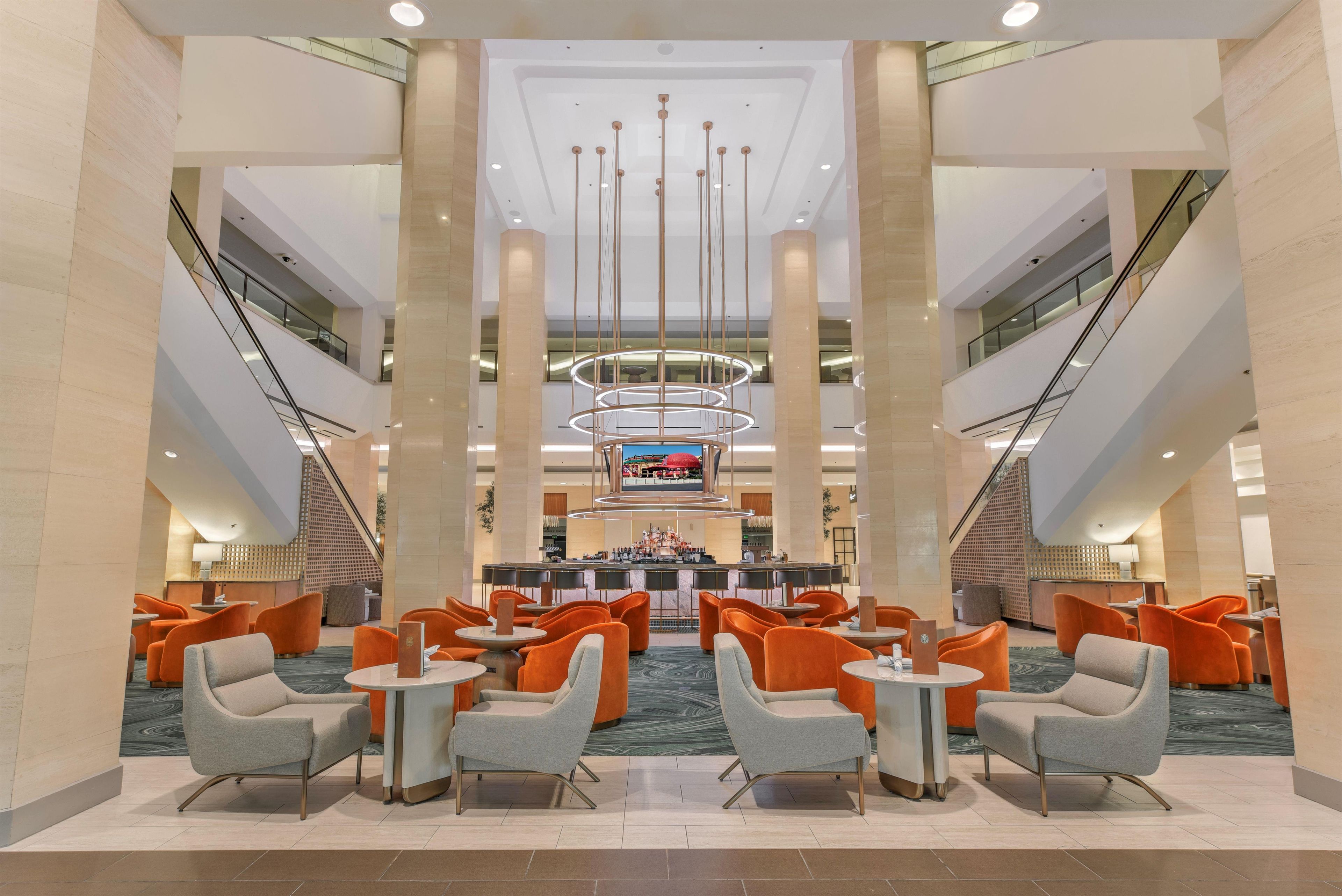 A hotel lobby with a central bar area, multiple seating options, and a modern chandelier.