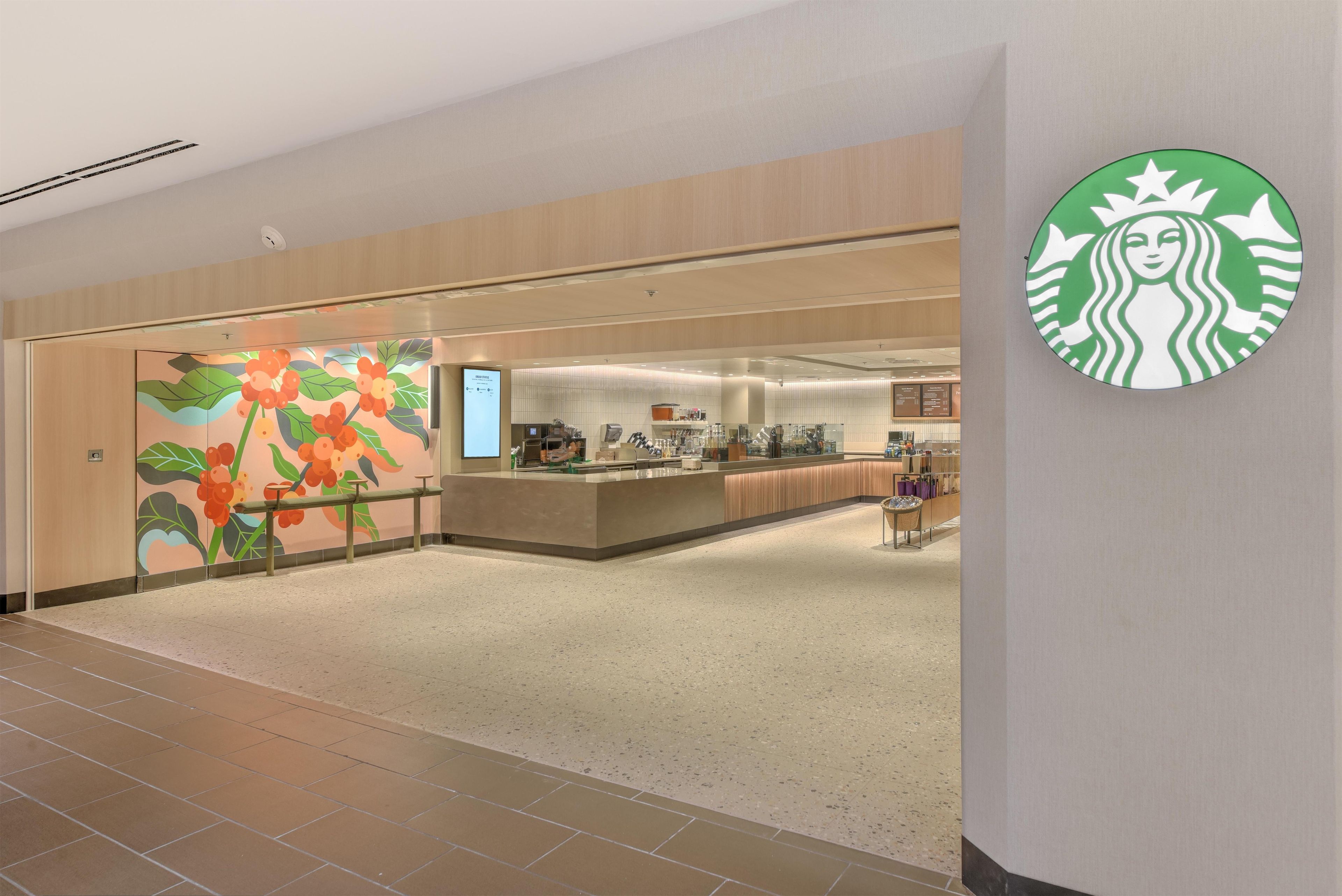 Un pasillo amplio con una cafetería Starbucks, un área de descanso y una pared con un mural colorido.
