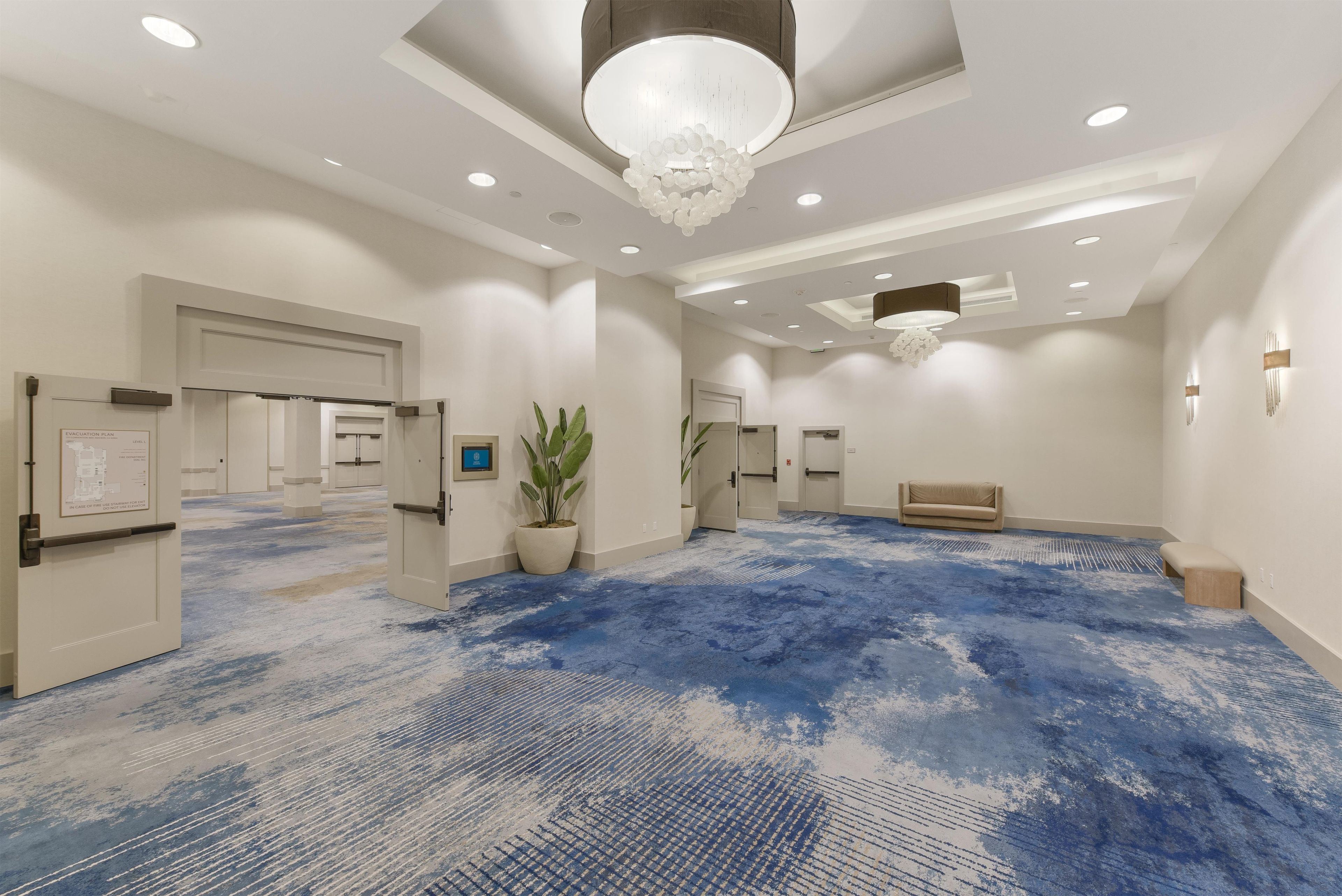 A spacious lobby with a blue patterned carpet, recessed lighting, a chandelier, and a reception desk.