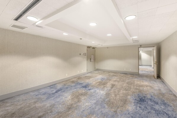 A spacious hallway with a textured carpet, recessed lighting, and a door leading to another room.