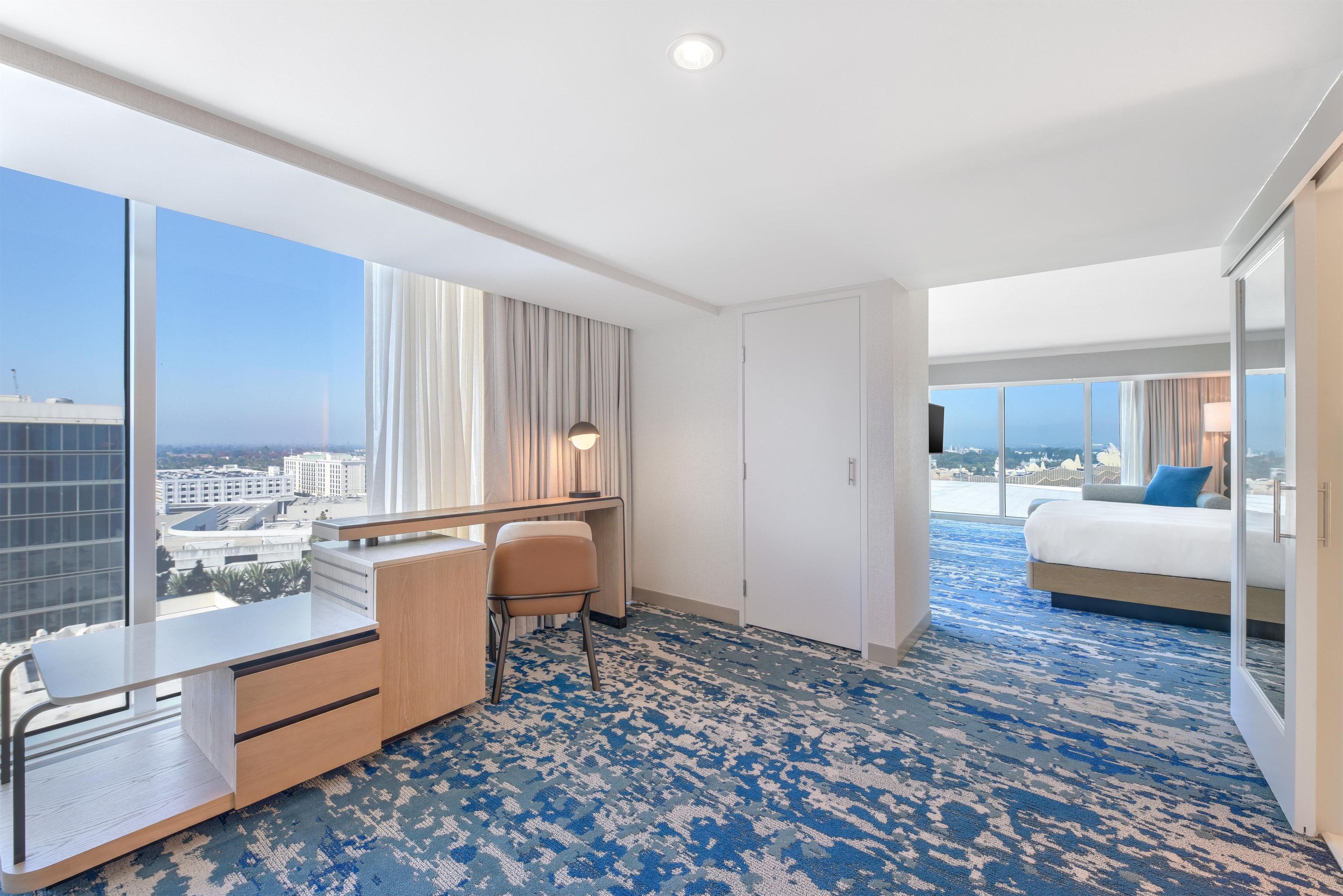 Una habitación de hotel con un ventanal grande, un escritorio, una silla, una cama y vistas a la ciudad.