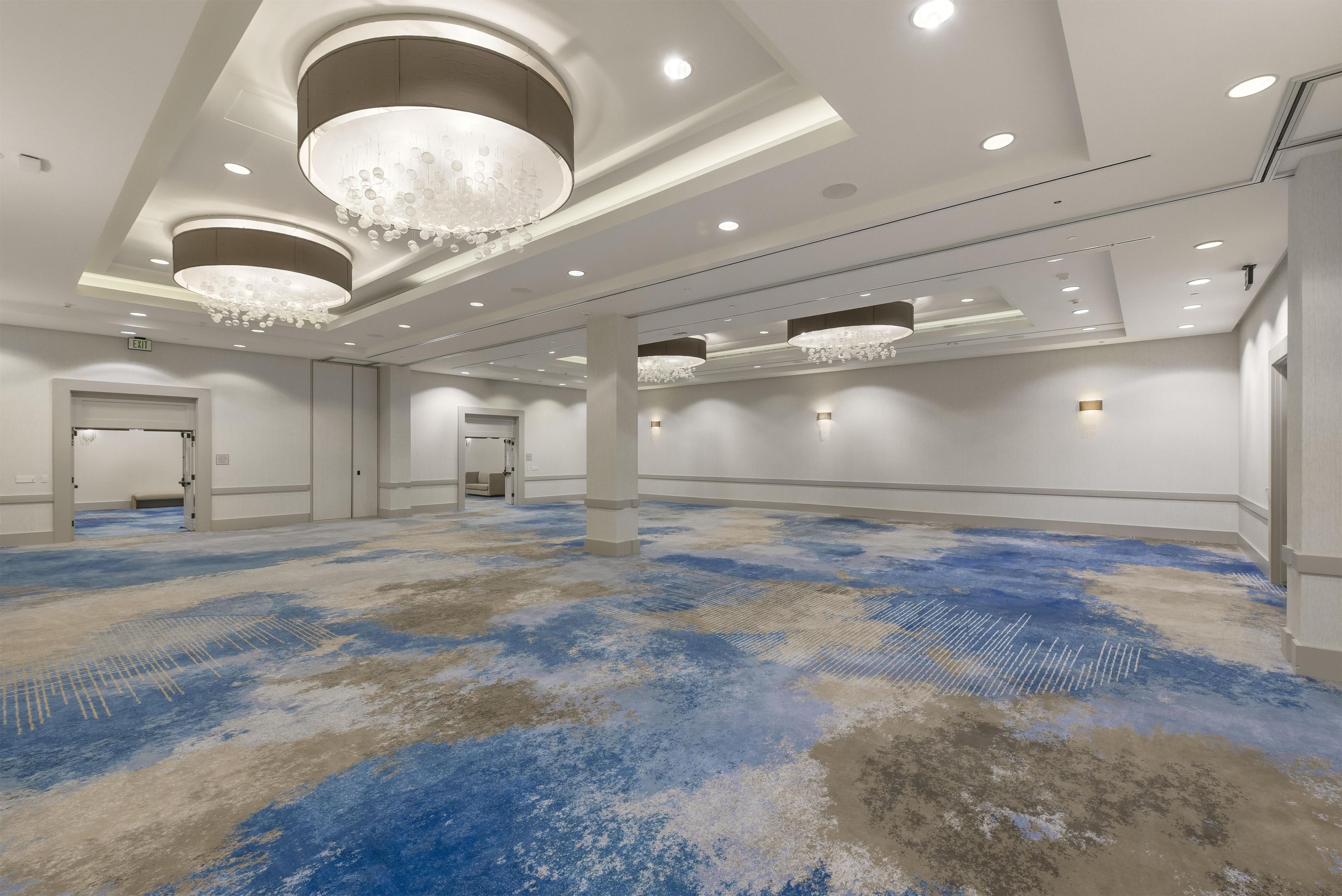 Un espacioso vestíbulo de hotel con alfombra estampada, iluminación empotrada y un candelabro.