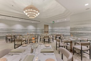 A spacious dining area with multiple tables set for service, a modern chandelier, and a wall mural.