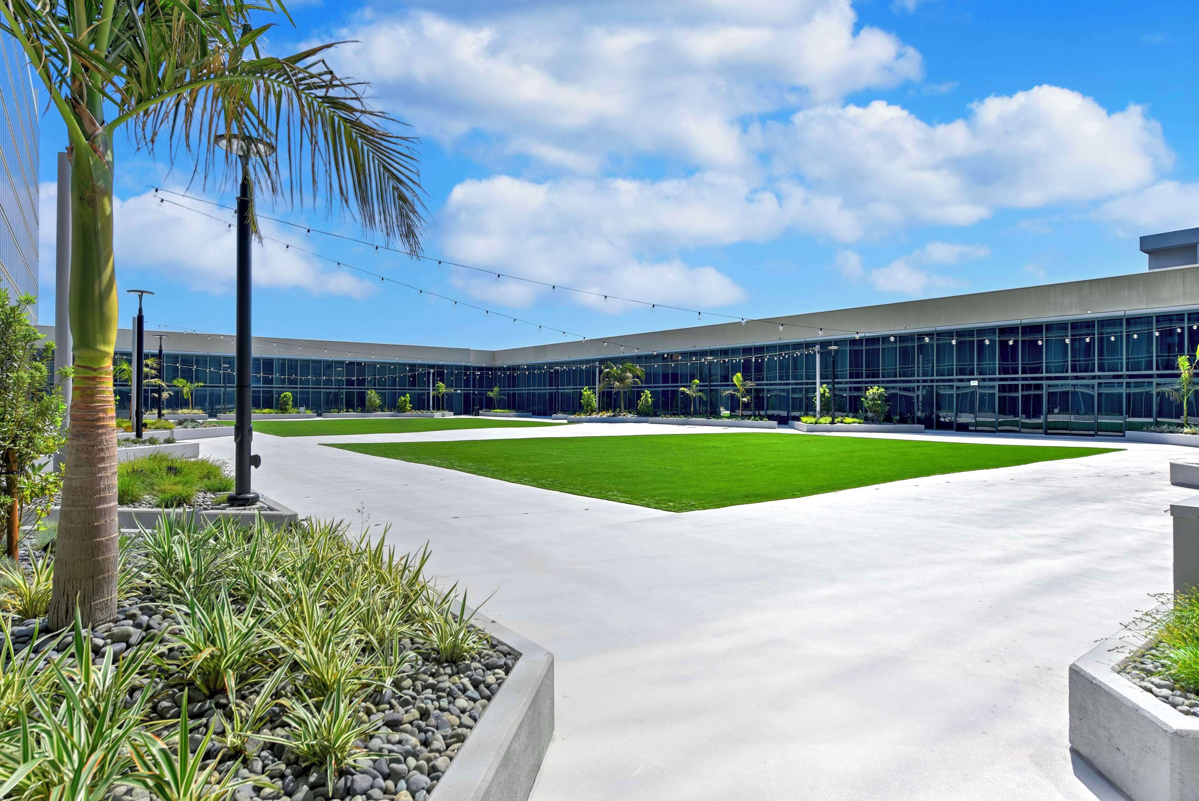 A modern building with a glass facade, a central lawn, and landscaped areas with plants and rocks.