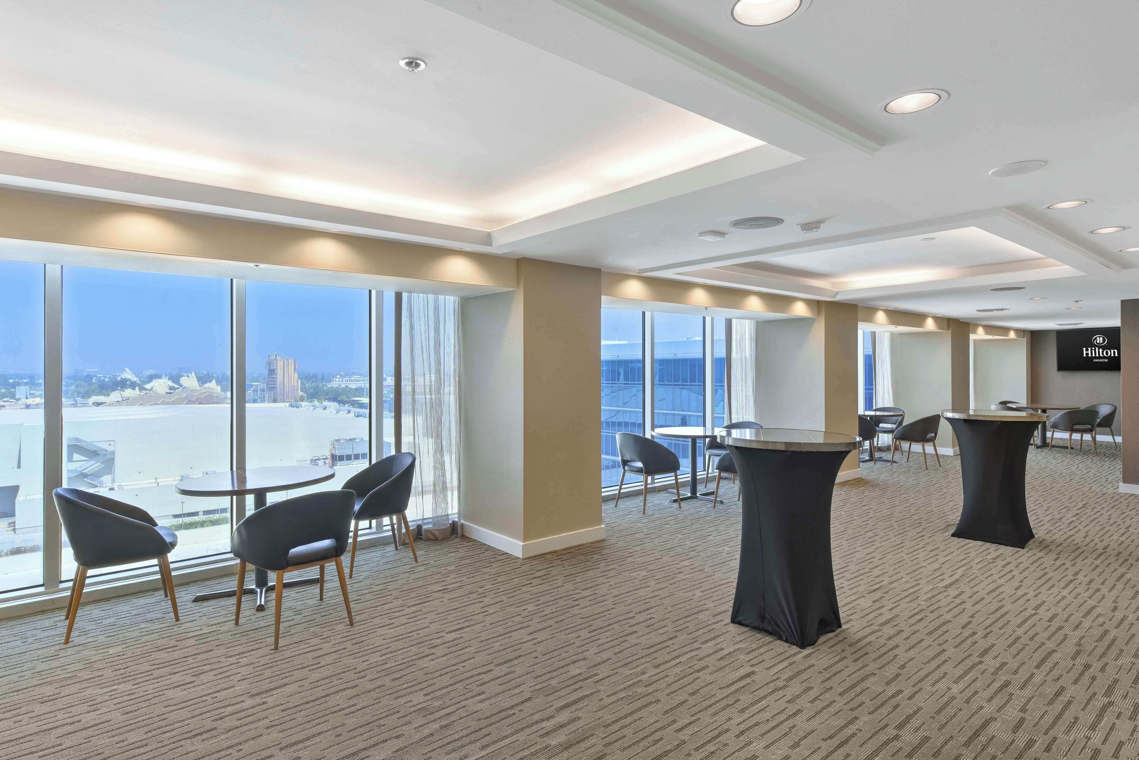 A hotel lobby with large windows, round tables, and chairs.