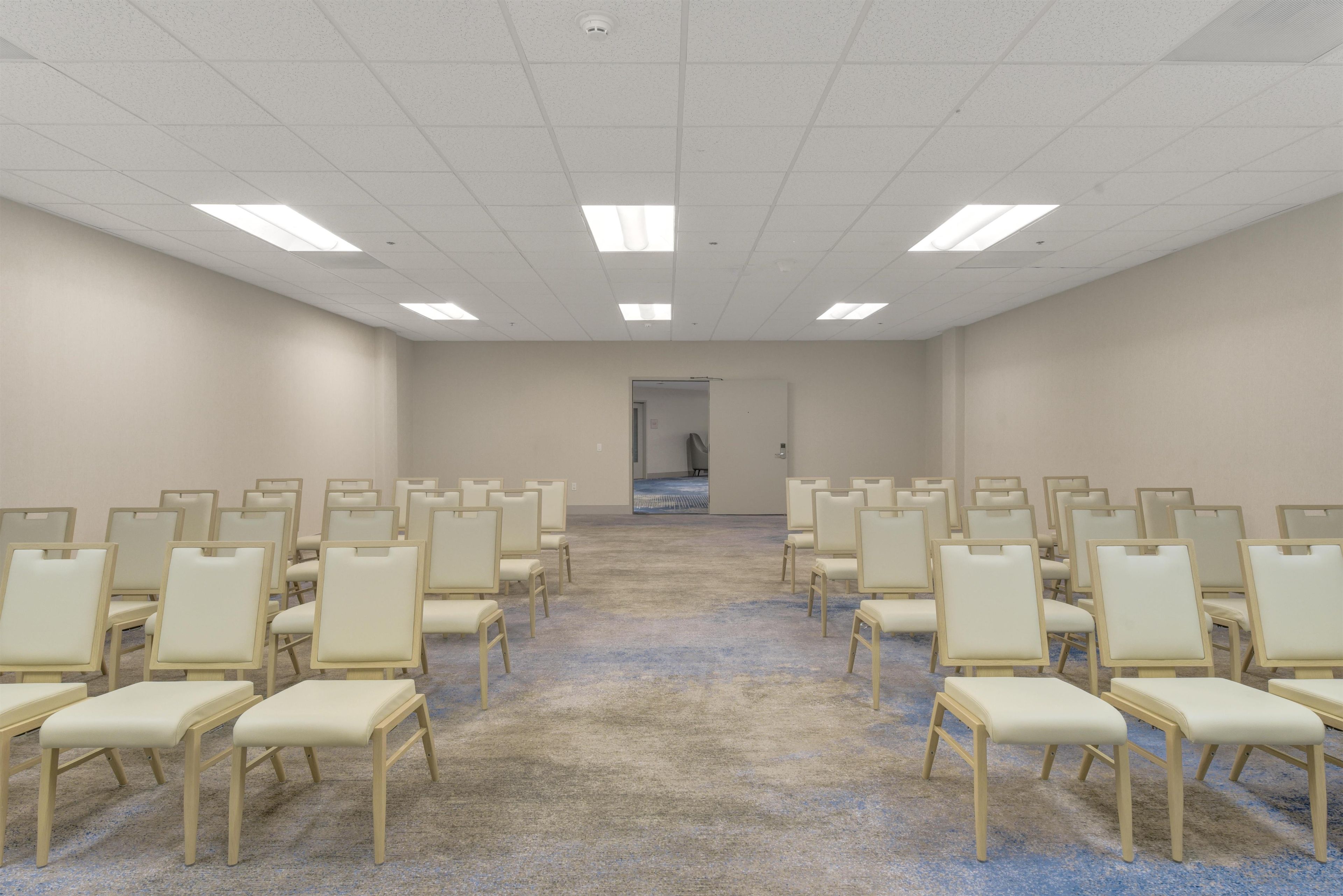 Un salón de conferencias con filas de sillas, piso alfombrado y una puerta al fondo.