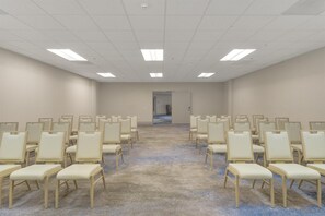 Une salle de conférence avec des rangées de chaises, un sol recouvert de moquette et une porte au fond.